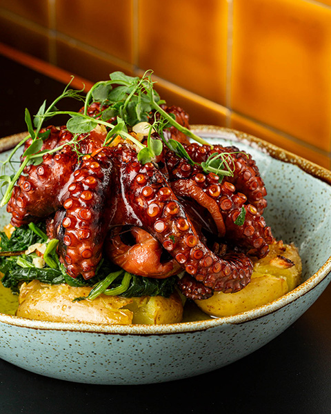 Um prato de Polvo com batatas e grelos em um prato sobre uma mesa de um restaurante