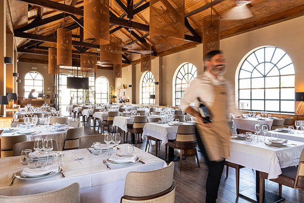 Um empregado de mesa a passar com uma garrafa de vinho entre as mesas de um restaurante.