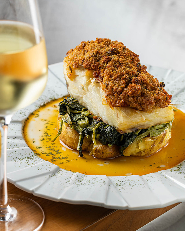 Um prato de bacalhau com grelos e batatas a murros com um copo de vinho